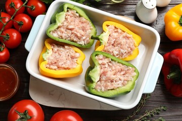 Raw stuffed peppers in dish and ingredients on wooden table, flat lay