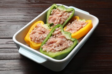 Raw stuffed peppers in dish on wooden table, closeup