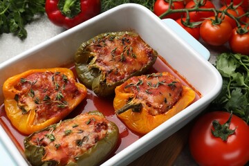 Tasty stuffed peppers in dish and ingredients on table, closeup