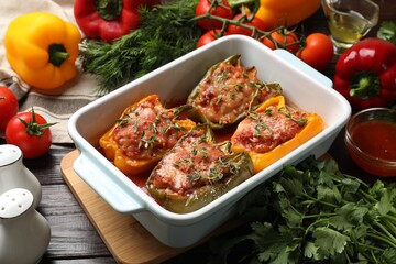 Tasty stuffed peppers in dish and ingredients on wooden table