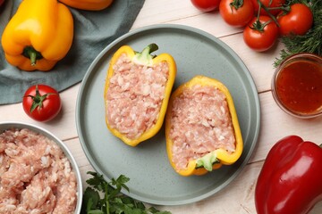 Raw stuffed peppers with ground meat and ingredients on light wooden table, flat lay