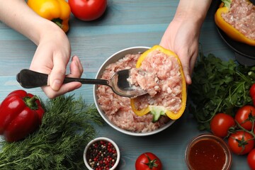 Woman making stuffed peppers with ground meat at light blue wooden table, top view