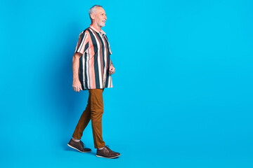 Full length photo of smiling sucessful retired man wear striped trendy clothes walk empty space isolated on blue color background