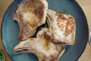 Top-down view of three cooked pork chops on a blue plate. The chops are beautifully seared, showing...