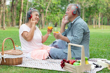 senior couple have a picnic wearing headphone to listen a music and holding orange juice glass in the park