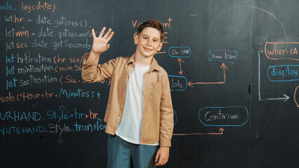Panorama shot of happy caucasian boy smiling and waving hand at blackboard with engineering code or...