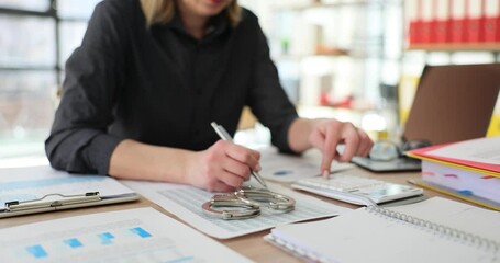 Woman employee counts income digits on calculator next to handcuffs sitting at workplace in room. Concept of breaking law and corruption in company slow motion