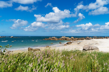 En premier plan, des lagunes ovales longent une plage jonchée de rochers massifs, sous un ciel bleu parsemé de magnifiques nuages blancs en Bretagne.