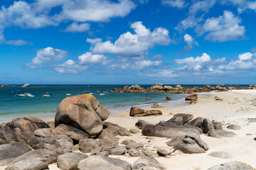 Sous un ciel bleu parsemé de nuages blancs, des eaux turquoise rencontrent des plages de sable et des rochers imposants.