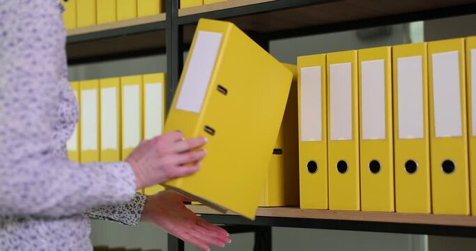 Woman hand takes yellow ring binder from office archive. Organized folder structure and archive on large rack in modern office slow motion