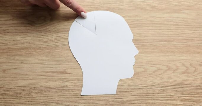 Woman hand puts missing triangular piece of human head paper shape on wooden table. Missing element as psychological concept of thinking on wooden board