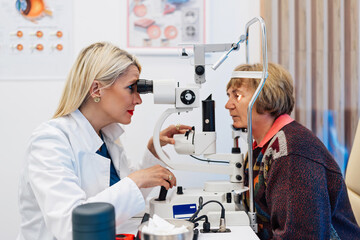 Beautiful female doctor ophthalmologist is checking the eye vision of senior woman in a modern clinic. Doctor and patient during medical check up in ophthalmology clinic.