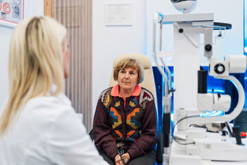 Beautiful female doctor ophthalmologist is checking the eye vision of senior woman in a modern...