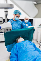 Skilled female surgeon and his medical team performs precise eye surgery on an elderly patient,...