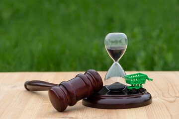 Hourglass, judge's gavel and miniature shopping cart from a supermarket on a wooden surface