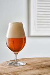A glass of amber red Belgian beer on a wooden table  against closed window with shutters. Shallow depth of field