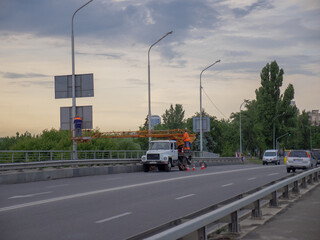 Truck-mounted elevating work platform with two workers doing their job on a road bridge in Kyiv capital city in the evening.