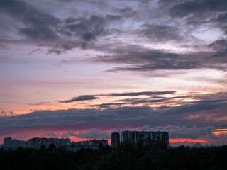 Colorful sunset over Kyiv city with buildings on the horizon. Industrial cityscape against the backdrop of setting sun with red and lilac scenic clouds.