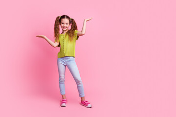Full length photo of lovely little girl hold compare empty space dressed stylish green garment isolated on pink color background