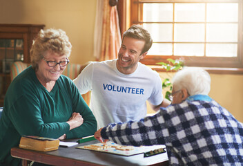Volunteer, man and happy with senior people in retirement home, board game and social interaction...