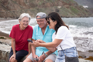Group of senior Caucasian friends in leisure travel at sea sitting looking together at mobile...