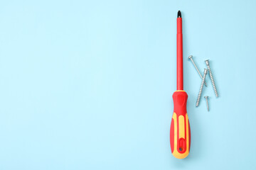 Screwdriver with red handle and screws on light blue background, flat lay. Space for text
