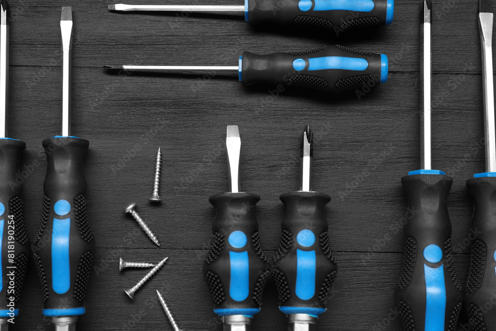 Poster Set of screwdrivers and screws on black wooden table, flat lay