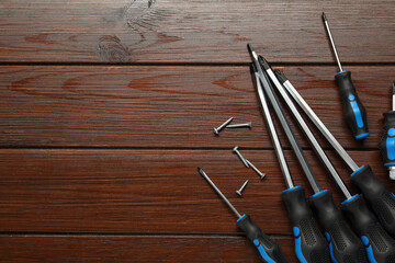 Set of screwdrivers and screws on wooden table, flat lay. Space for text