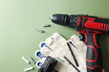 Electric screwdriver, gloves and accessories on pale green background, flat lay