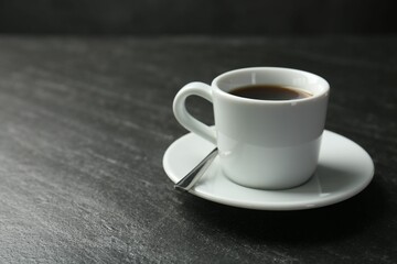 Hot coffee in cup and saucer on dark textured table, closeup. Space for text