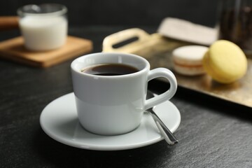 Hot coffee in cup, saucer and spoon on dark textured table, closeup