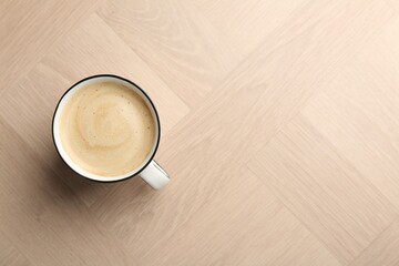 Tasty cappuccino in cup on light wooden table, top view. Space for text