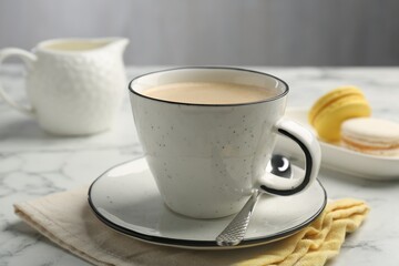 Tasty cappuccino in cup, spoon and saucer on white marble table, closeup