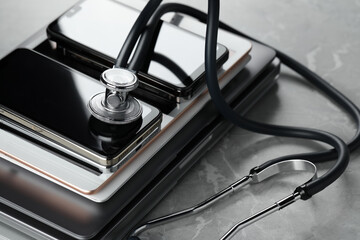 Stack of electronic devices and stethoscope on grey table, closeup