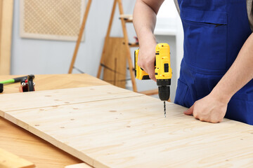 Young worker using electric drill at table in workshop, closeup