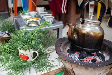 A jebena sits on a grass-covered table with small, handle-less cups arranged around it. Roasted coffee beans, a mortar and pestle, and incense smoke create a traditional Ethiopian coffee ceremony