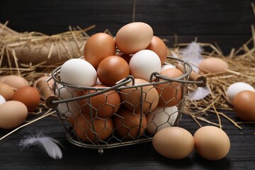 Fresh chicken eggs and dried straw on black wooden table