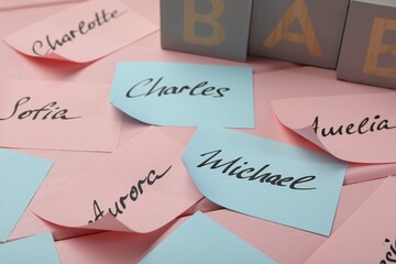 Paper stickers with different names on pink wooden table, closeup. Choosing baby's name