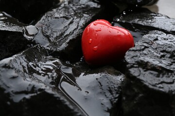 Red decorative heart on stones and water, closeup. Space for text
