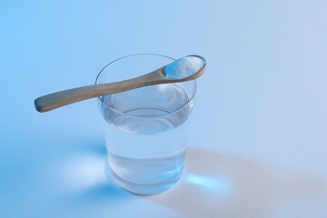 Glass of water and spoon with baking soda on light blue background. Space for text