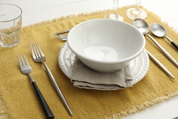 Stylish setting with cutlery, dishes and napkin on white wooden table