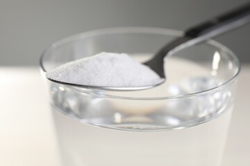 Glass of water and spoon with baking soda on color background, closeup