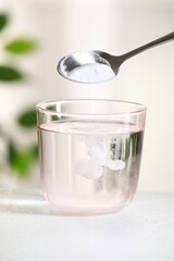 Adding baking soda into glass of water at white table against blurred background