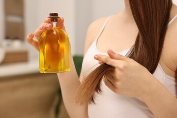 Natural hair mask. Woman holding bottle of oil at home, closeup