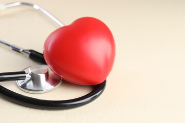 Stethoscope and red heart on beige background, closeup. Space for text