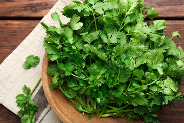 Fresh coriander in bowl on wooden table, top view