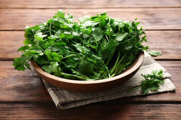 Fresh coriander in bowl on wooden table, closeup