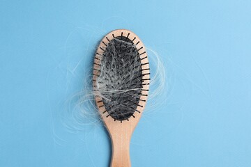 Wooden brush with lost hair on light blue background, top view