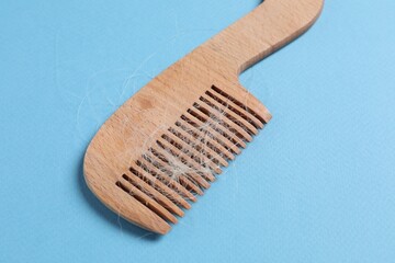 Wooden comb with lost hair on light blue background