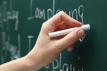 English teacher writing with chalk on green chalkboard, closeup
